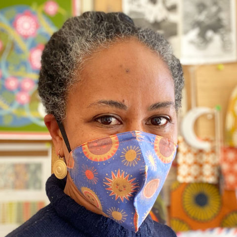 Photo of Jen Hewett wearing a mask made with fabric printed with her Many Suns illustration